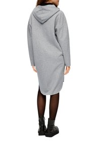 Šedé mikinové šaty s kapucí, volný střih, dlouhé rukávy a zaoblený lem. Nosené s černými kotníkovými botami a poloprůhlednými punčochami.