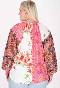 Blusa multicolore con motivi floreali e paisley, con scollo arr gathered, maniche lunghe e un mix di tessuti vibranti in rosa, bianco e nero.
