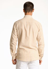 Gestreepte langemouwen shirt in beige en wit, met een button-down kraag en afgeronde zoom. Heeft schouderplooien en knopenmanchetten.