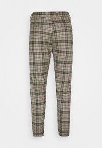 Pantaloni a quadri in beige, oliva e nero. Presentano una gamba affusolata, una vita elastica e due tasche posteriori con cuciture decorative.