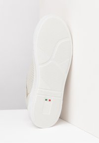 Baskets blanches avec une semelle en caoutchouc texturée, dotées d'un système de laçage et d'accents en maille. Marquées "NeroGiardini" avec un détail du drapeau italien.