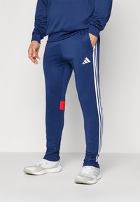 Navy athletic pants made of stretch material, featuring white stripes down the sides and a red accent on the lower leg.