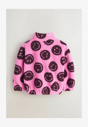 Rozā krāsas flīsa džemperis ar melniem smaidiņa rakstiem. Aprīkots ar augstu apkakli un elastīgiem aprocēm, lai radītu pieguļošu formu. Mīksta tekstūra.