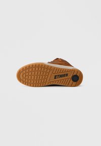 Donji dio smeđe tenisice s teksturiranim gumenim potplatom. Sadrži logo Etnies, gazni sloj za prianjanje i kontrastni svjetliji sloj.