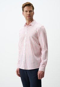 Chemise blanche à manches longues avec des rayures verticales rouges fines, col boutonné et poignets avec un motif de rayures assorti.