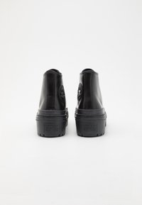 Pár černých vysokých tenisek Converse All Star zobrazených zezadu na bílém pozadí.