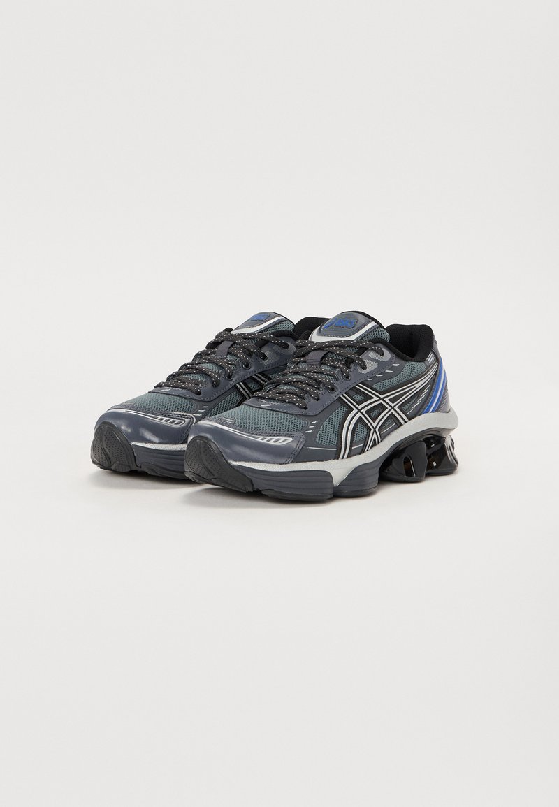 Zapatillas deportivas con parte superior de malla en tonos de gris y negro, que cuentan con acentos reflectantes, cordones texturizados y una suela acolchada.
