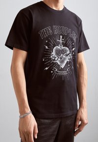 Camiseta de algodón negra con un estampado gráfico de un corazón estilizado con una espada y rayos; corte relajado con mangas cortas.
