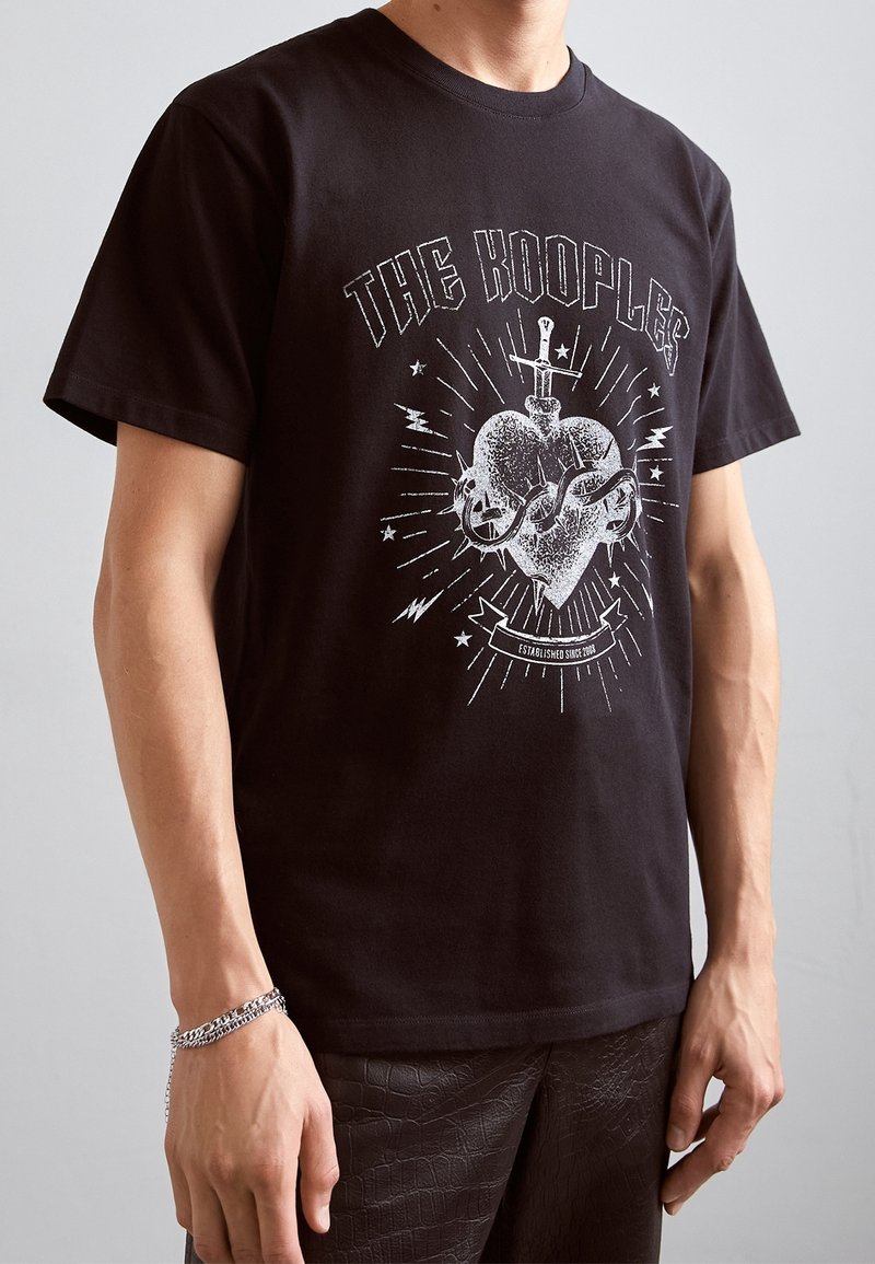 Camiseta de algodón negra con un estampado gráfico de un corazón estilizado con una espada y rayos; corte relajado con mangas cortas.