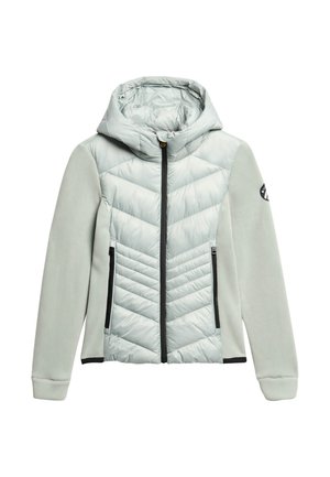 Veste à capuche gris clair avec un mélange de tissu matelassé et lisse. Elle dispose d'une fermeture éclair à l'avant, d'un motif en chevrons et de poches latérales avec des zippers.