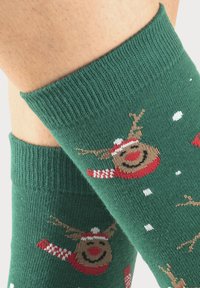 Grüne Socken mit einem gestrickten Design von Rentieren mit roten Schals, weißen Schneeflocken und gerippten Bündchen. Weiches, strukturiertes Material.