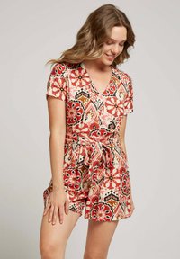 Rompers à imprimé floral en crème, avec des motifs rouges, noirs et orange. Manches courtes, décolleté en V et un détail de taille nouée avec des shorts.