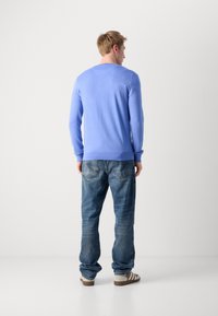 Hellesblaues langärmliges Sweatshirt mit Rundhalsausschnitt, kombiniert mit blauen Jeans aus Denim und beigen Sneakers. Glatte Textur, anliegendes Design.