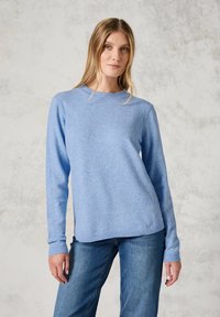 Helles blaues Strickpullover mit langen Ärmeln und Rundhalsausschnitt, ausgestattet mit gerippten Bündchen und Saum. Kombiniert mit blauen Jeans.