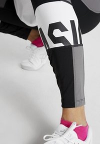 Leggings in bianco e nero con una grande stampa grafica e dettagli grigi. Abbinati a sneakers bianche e calzini alla caviglia rosa.