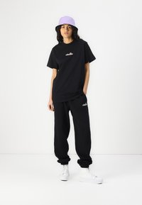 Sort t-shirt og matchende joggers med broderet logo, sat sammen med en lilla bøttehat og hvide sneakers. Afslappet pasform, bomuldsstof.