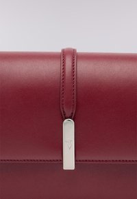 Bordeaux leren tas met een gladde textuur, voorzien van een zilveren metalen sluiting en gestikte details op de klep.