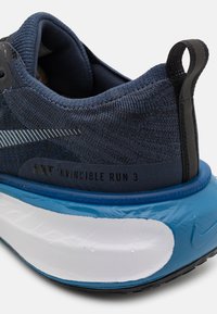 Pantofii de alergare navy cu partea superioară texturată, talpă intermediară albă și albastră, toc mare cu amortizare și accente negre. Prezintă brandingul "Nike Invincible Run 3".