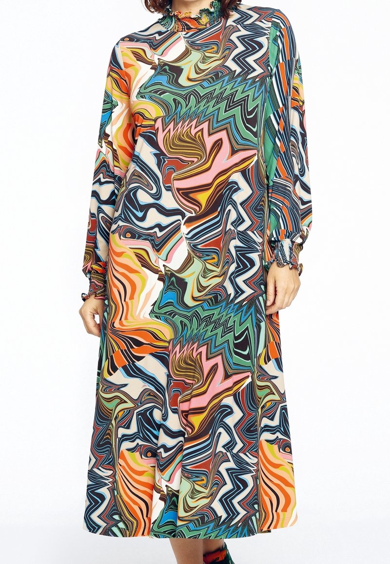 Femme portant une robe à manches longues et col haut avec un motif tourbillonnant abstrait et coloré en nuances d'orange, vert, bleu, rose et noir.