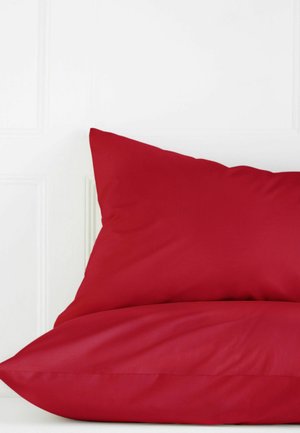 Zwei rote Kissen, übereinander gestapelt auf einer weißen Oberfläche mit einer schlichten weißen Wand im Hintergrund.
