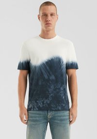 Baumwoll-T-Shirt mit einem blauen Batikmuster am Saum, das von Cremefarben zu marineblau übergeht. Kurze Ärmel und runder Halsausschnitt.