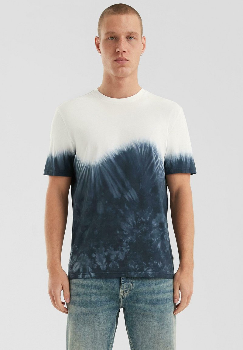 Baumwoll-T-Shirt mit einem blauen Batikmuster am Saum, das von Cremefarben zu marineblau übergeht. Kurze Ärmel und runder Halsausschnitt.