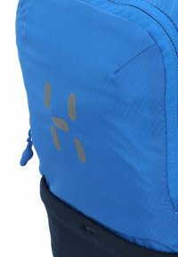 Zaino blu con un tessuto a trama texturizzata a motivo diamante. Presenta una base nera e un dettaglio logo riflettente sulla parte frontale. Chiusura con cerniera.