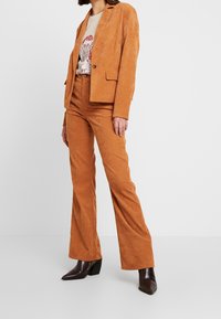 Brun kordflor kostym med en strukturerad kavaj och utsvängda byxor. Tyget har en texturerad yta och är kombinerat med svarta klackstövlar.