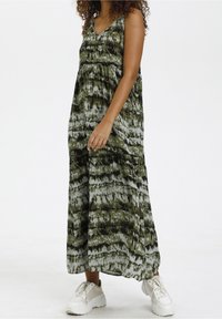 Robe maxi dans un motif abstrait vert et gris, en tissu doux avec un décolleté en V et une coupe décontractée, associée à des baskets blanches.