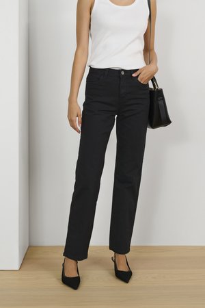 Black high-waisted jeans with a straight-leg cut, paired with a white tank top. Black handbag and pointed-toe heels complete the look.
