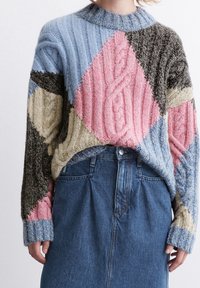 Stickad tröja med en lapptäckesdesign i blå, rosa, brun och beige sektioner; ribbat mönster; hög krage; bärs över en jeanskjol.