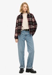 Koszula z flaneli w bordowo-kremową kratę, założona na beżowy sweter, w połączeniu z jasnoniebieskimi dżinsami z wysokim stanem i czarnymi butami na sznurowadła.