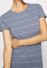 T-shirt bleu rayé avec un col rond, des manches courtes et un tissu doux et texturé. Les rayures sont blanches sur un fond chiné.