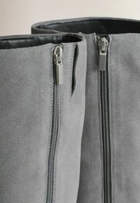 Gray suede boots featuring dual zippers, a smooth interior lining, and a sleek silhouette. The exterior showcases a soft, textured finish.