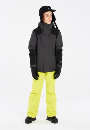 Veste de ski grise avec des accents noirs, dotée d'un col haut et d'une poche. Associée à un pantalon de neige jaune vif, des gants noirs et des bottes.
