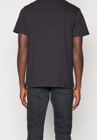 Camiseta de algodón negra con mangas cortas y dobladillo recto. Vista trasera que muestra una textura suave y un diseño simple. Sin logotipos ni patrones visibles.