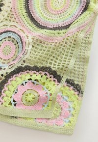 Tissu crocheté avec des motifs floraux circulaires en rose pastel, vert, bleu et marron reliés par une maille ouverte.