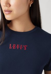 Mornarsko modra bombažna majica s rdečim vezenim logotipom "LEVI'S" na prsih, s klasičnim okroglim izrezom in gladko teksturo.