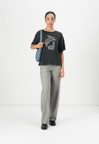 Black oversized t-shirt with rabbit graphic, gray wide-leg trousers, and black shoes. Model carries a blue shoulder bag. Minimalist background.