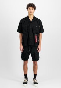 Zwarte T-shirt met korte mouwen en twee borstzakken, gecombineerd met zwarte cargo shorts met meerdere zakken, gedragen met zwarte sneakers.
