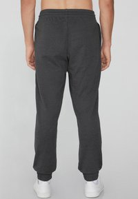 Dunkelgraue Sweatpants mit elastischem Taillenbund und Bündchen, aus einem glatten Material ohne sichtbare Logos oder Muster. Getragen mit weißen Schuhen.