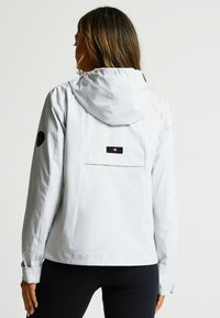 Light gray waterproof jacket with a hood, featuring a back pocket, logo patch on the sleeve, and elastic cuffs. Smooth texture.