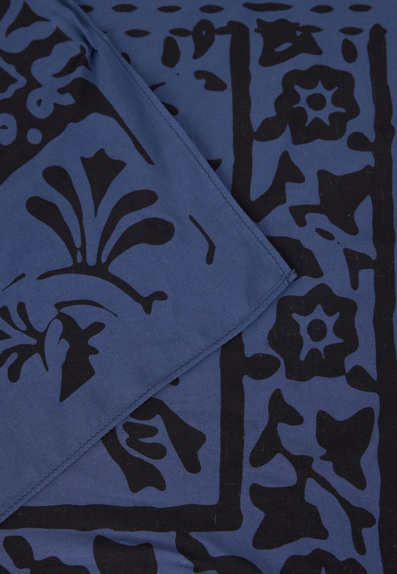 Blauer Stoff mit schwarzen floralen und abstrakten Mustern, Ränder gefaltet, um die Nahtdetails entlang des Randes zu zeigen.