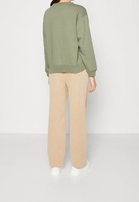 Felpa verde in cotone con una vestibilità morbida, abbinata a pantaloni beige a gamba larga e sneaker bianche. Mostrata da dietro.