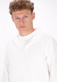 Hvid fleece sweatshirt med lynlås, der har en blød tekstur og en høj krave, designet til komfort og varme. Minimalistisk stil uden mønstre.