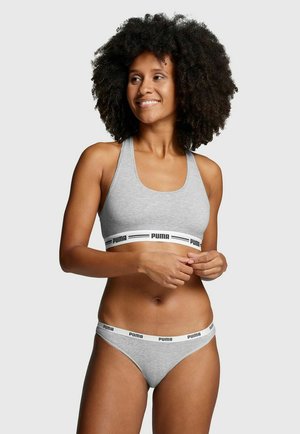 Grauer Sport-BH mit einem breiten schwarzen und weißen "PUMA" Logo-Band am unteren Rand; kombiniert mit grauer String-Unterwäsche, die ein ähnliches Banddesign aufweist.