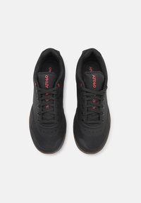 Black athletic shoes with red accents, featuring a mesh and synthetic material design, lace-up closure, and a textured brown sole.