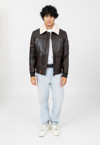 Bruine leren bombersjack met een crèmekleurige nepleer kraag, met voorzakken en geribbelde manchetten, gedragen met lichtblauwe jeans en witte sneakers.