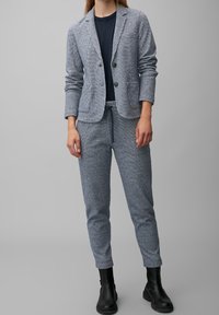 Světlý šedý texturovaný blazer se dvěma knoflíky, kombinovaný s odpovídajícími měkkými jogger pants a černými kotníkovými botami. Pod tím námořnické tričko.