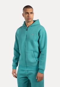 Felpa zip-up verde menta realizzata in tessuto morbido, con cappuccio foderato, tasche a marsupio e polsini e bordo a costine.